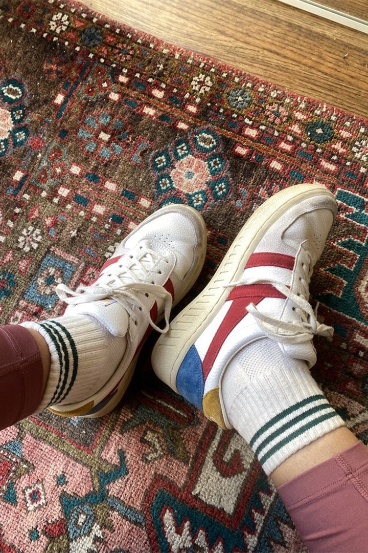 A person wears sneakers with striped green ankle socks