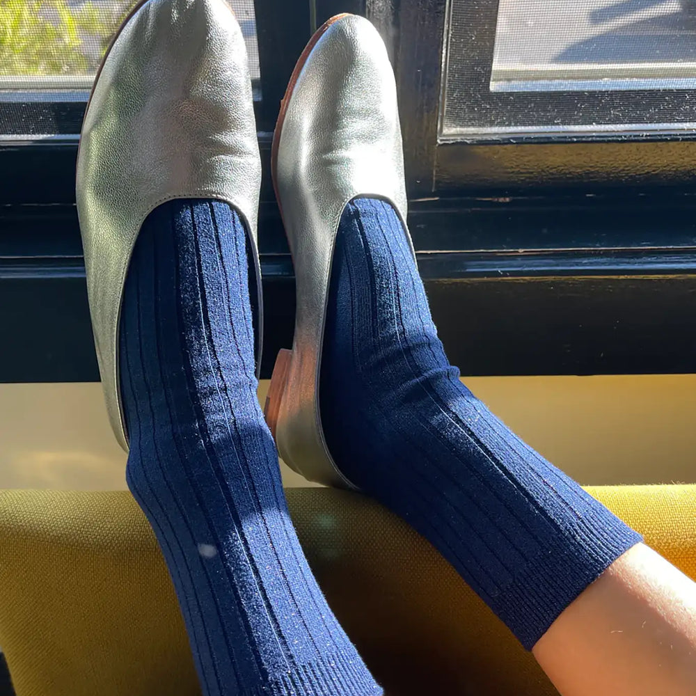 A pair of blue ribbed socks with glitter embellishments worn on someone's feet, displayed against a window.