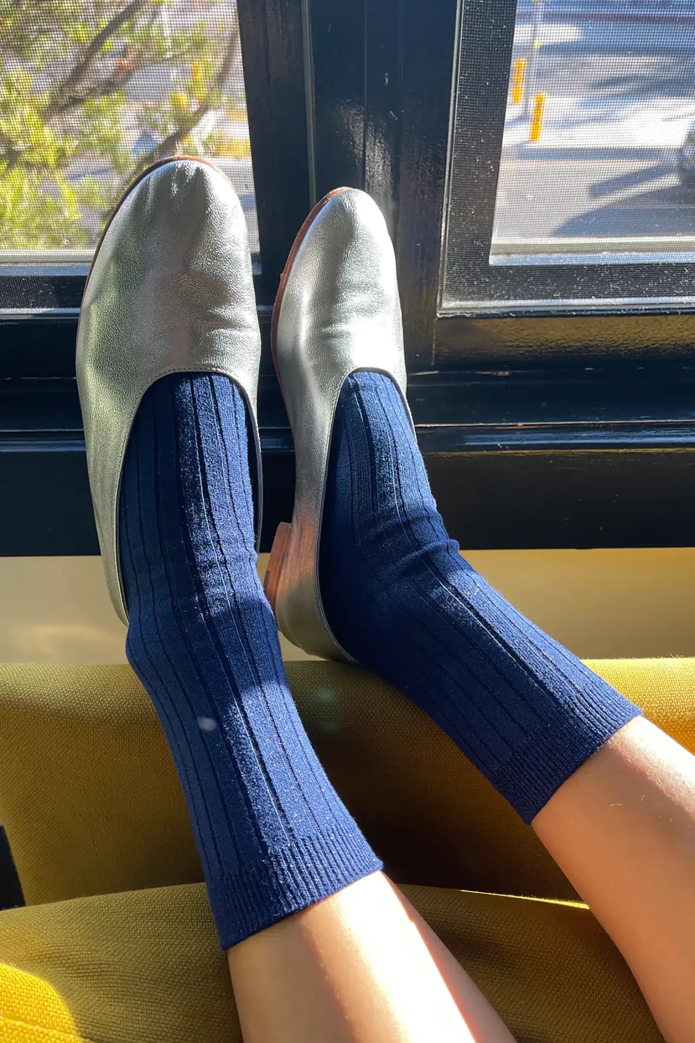 A pair of blue ribbed socks with glitter embellishments worn on someone's feet, displayed against a window.