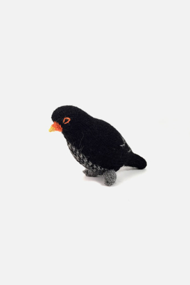 Hand-knit wool black bird bird toy with black body and orange beak, on a white background.