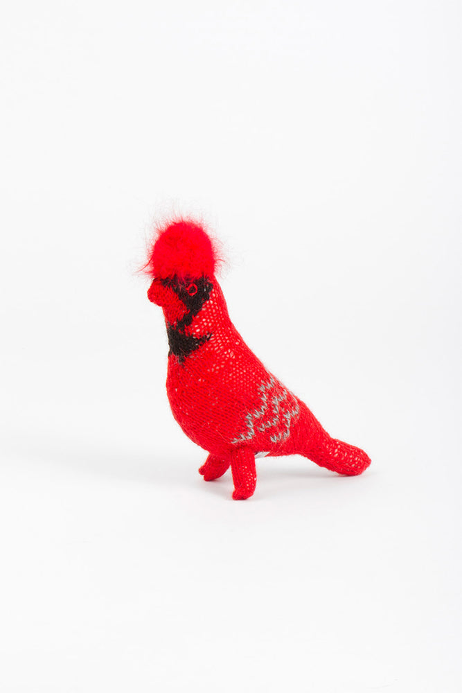 A hand-knit red cardinal bird with a black and white pattern on its chest and a fluffy tuft on its head, standing against a white background.