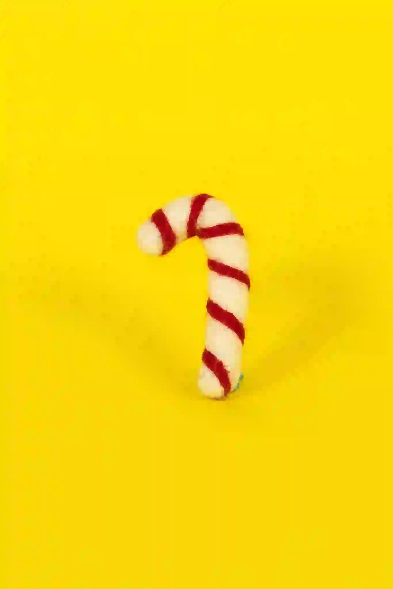 A candy cane-shaped cat toy made of lambswool with a red and white striped design, displayed on a yellow background.