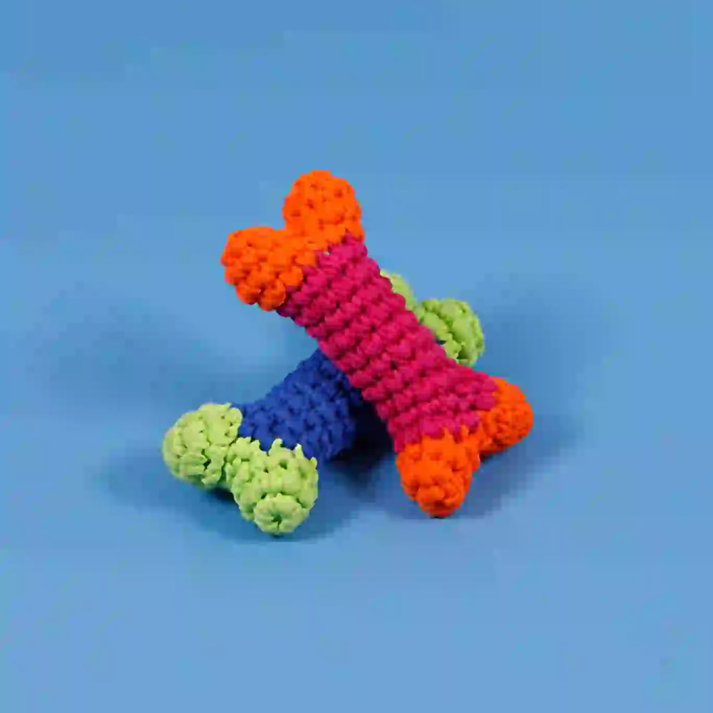 A crochet dog bone toy in blue, green, and orange colors laid on a blue background.