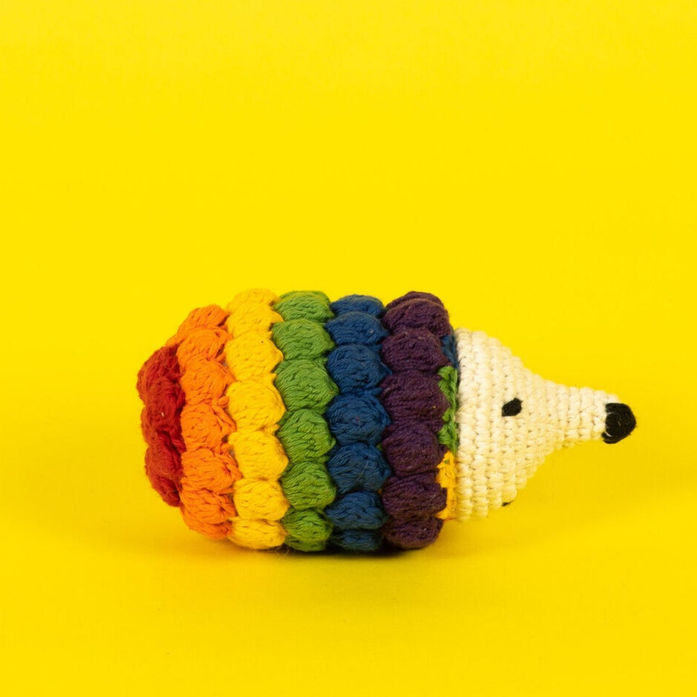 A rainbow felted hedgehog dog toy on a yellow background.