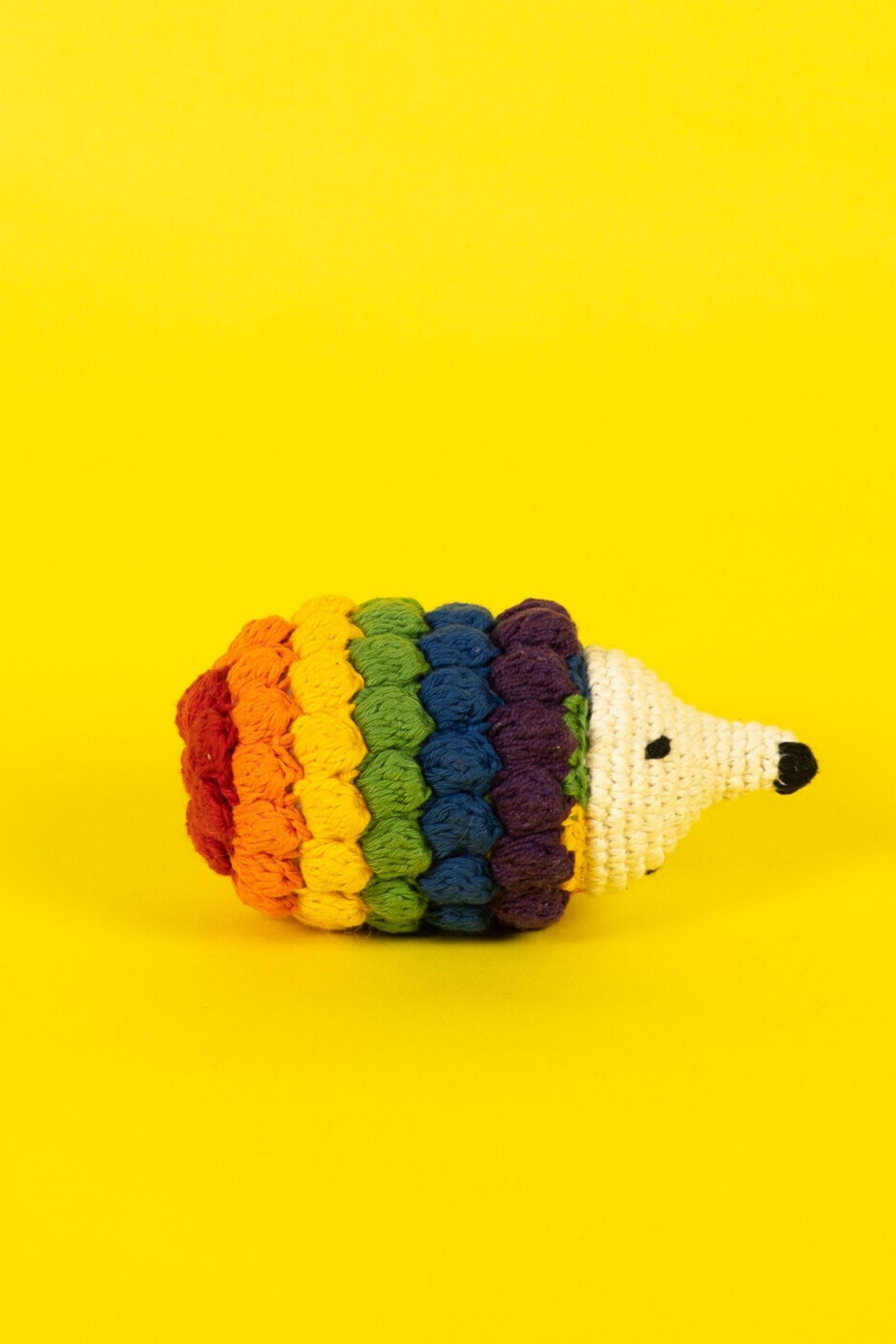 A rainbow felted hedgehog dog toy on a yellow background.