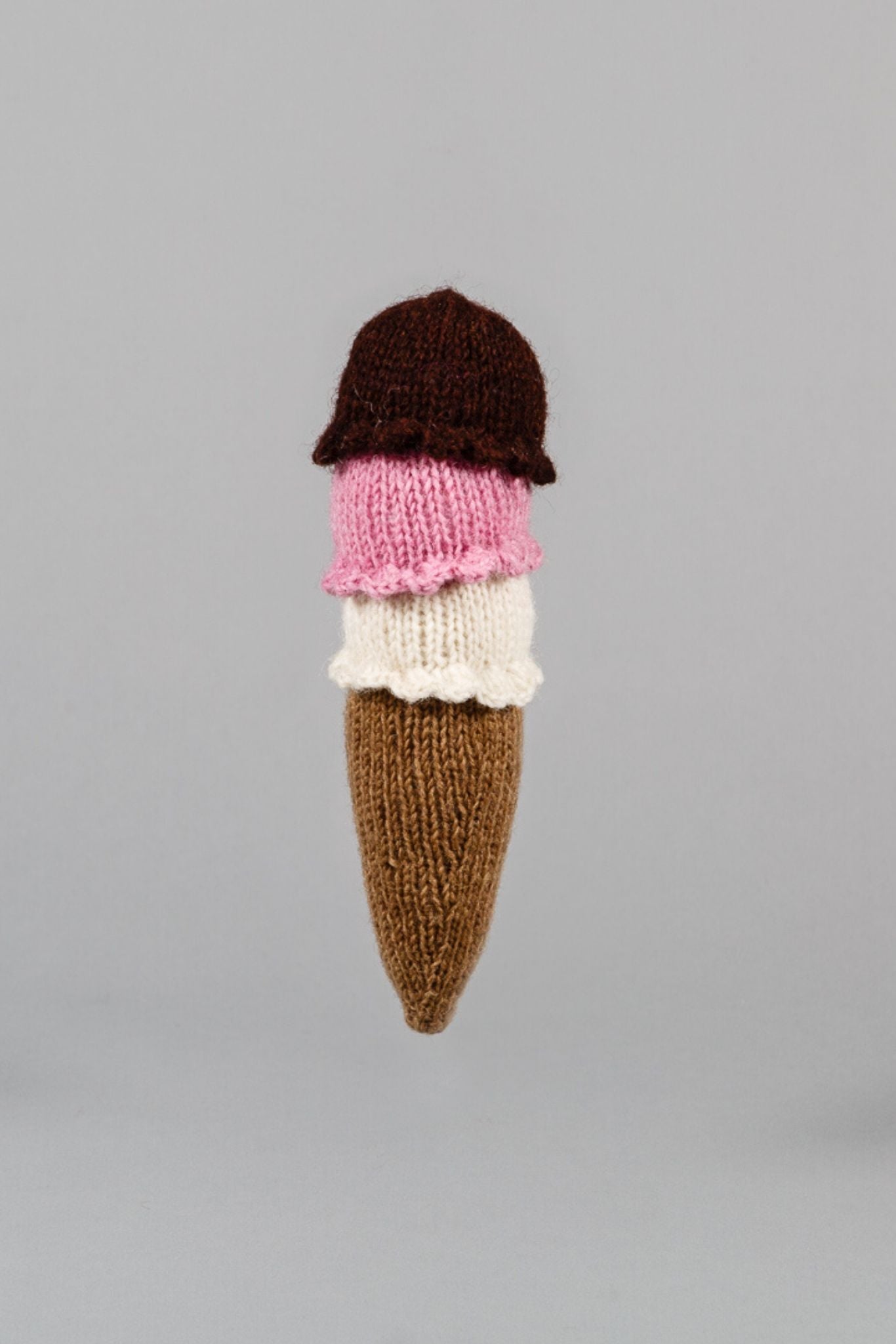 A hand knit dog toy shaped like an ice cream cone with brown, pink, and white colors.