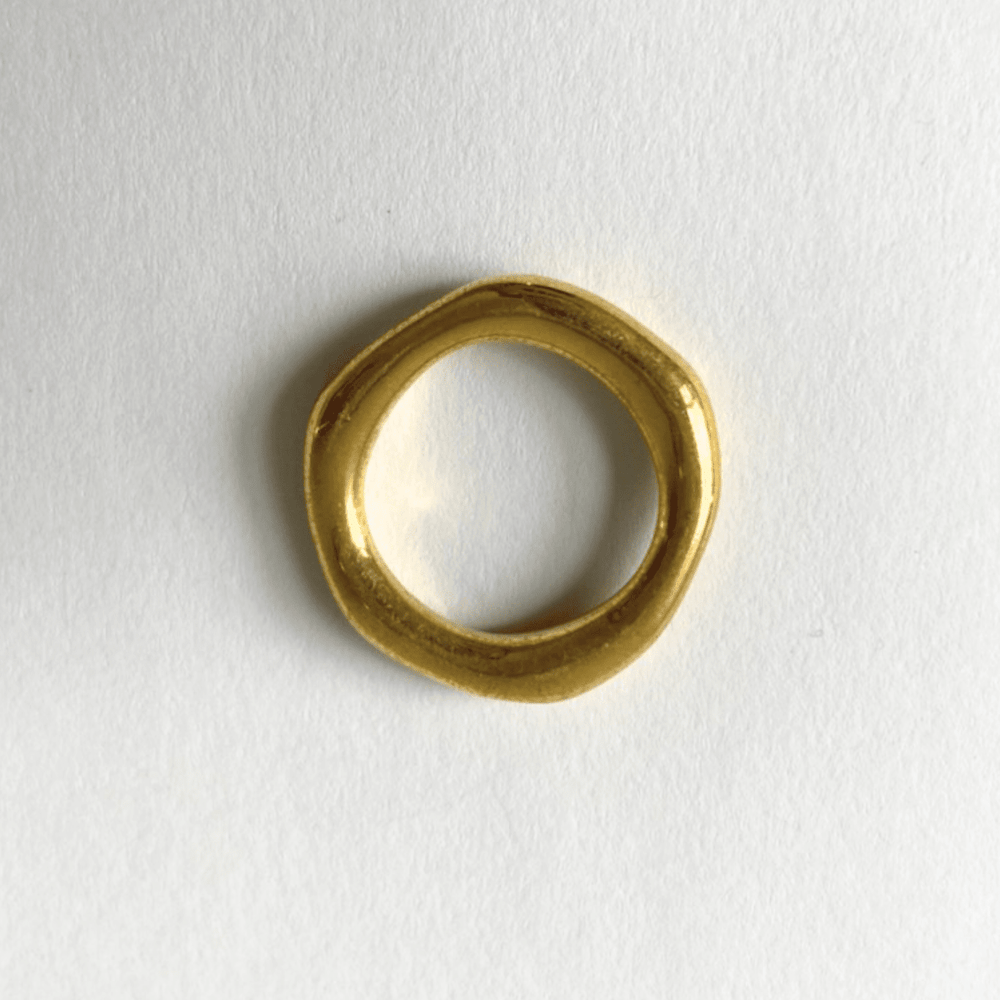 The birds eye view of a simple gold brass organic band ring on a white background.