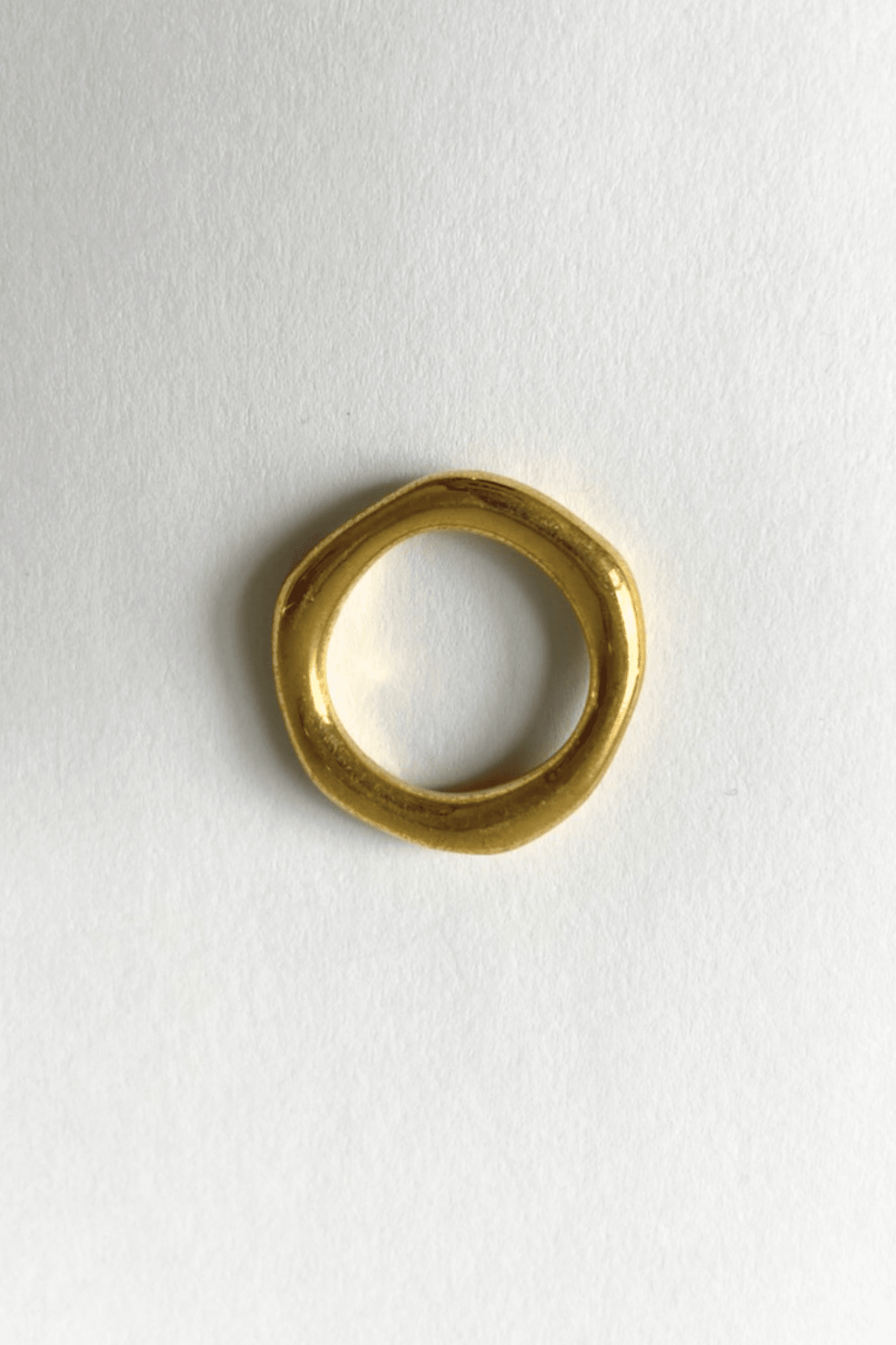 The birds eye view of a simple gold brass organic band ring on a white background.