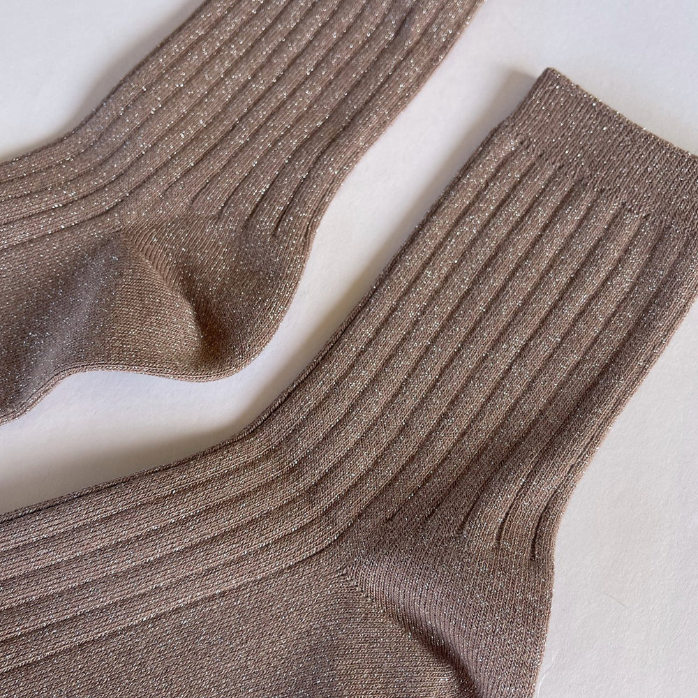 A close up view of ribbed socks in a rose gold color with glitter embellishment, displayed against a white background.