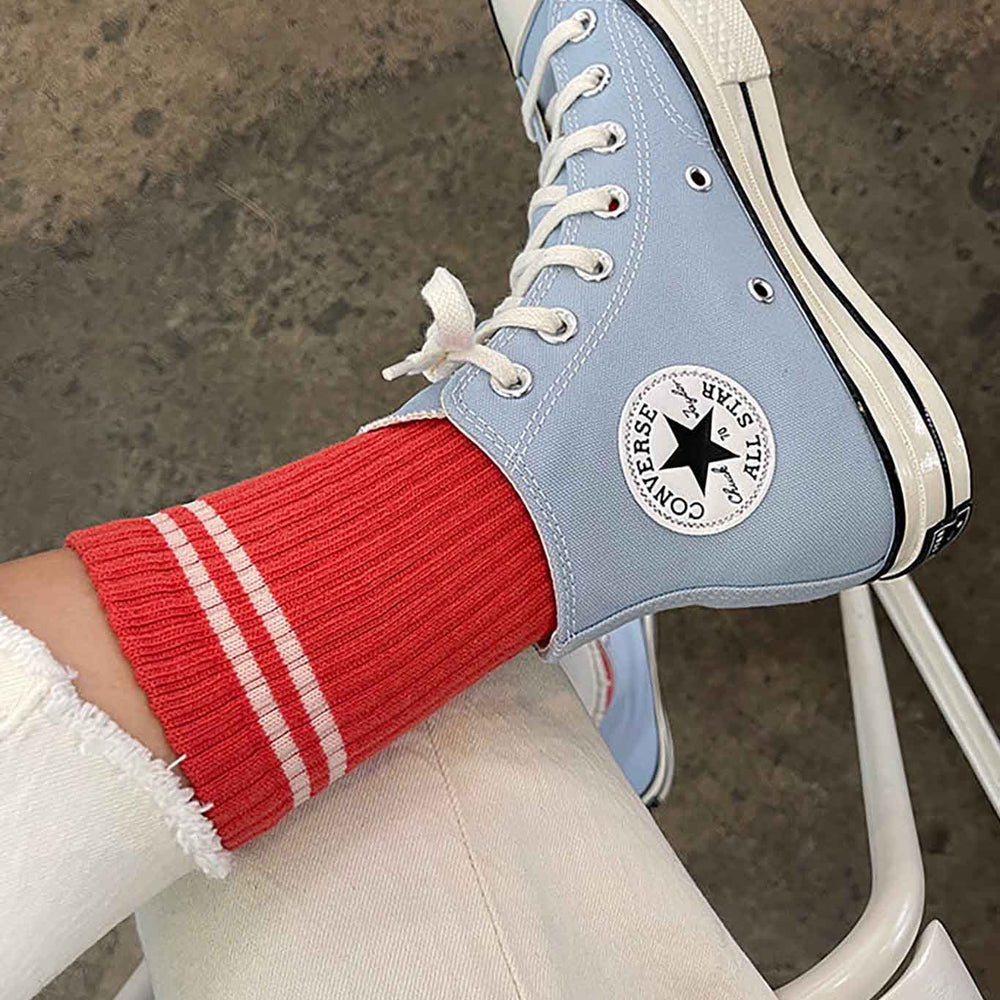 Person wearing coral red crew socks with white stripes and blue converse