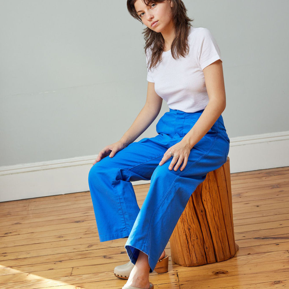 
                  
                    A woman sitting wearing a white t-shirt and cobalt blue high-rise wide-leg crop sailor pant with front pockets.
                  
                